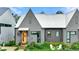 Home's grey exterior featuring an orange front door, metal roof, lush landscaping, and white Adirondack chairs at 10862 Serenbe Ln, Chattahoochee Hills, GA 30268