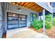 Garage with glass panel door and stained wood beams on the ceiling; landscaped with plants and pine straw at 10862 Serenbe Ln, Chattahoochee Hills, GA 30268