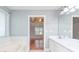 Bathroom featuring tiled soaking tub, double sink vanity, and view into a bedroom with trey ceilings at 3554 Cherry Blossom Court, Loganville, GA 30052