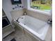 A close up of a bathtub features neutral tile and a window with backyard view at 188 Macedonia Rd, White, GA 30184