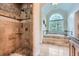 Elegant bathroom featuring a walk-in shower with decorative tiles, a soaking tub, and a large arched window at 4829 Moon Rd, Powder Springs, GA 30127