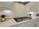 Close-up of a gas cooktop with a decorative backsplash, stainless steel range hood, and white countertops at 7310 Winderlea Ln, Cumming, GA 30040