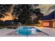 Backyard pool with a slide and hot tub surrounded by a large patio and mature trees at twilight at 3217 Aberrone Pl, Buford, GA 30519