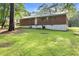 A grassy backyard with a brick house featuring white painted foundation and mature trees at 6671 Gano Dr, Riverdale, GA 30274