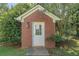 Quaint brick shed with a white door and trim, nestled in a lush, green yard with mature trees at 901 Chadwick Park Dr, Lawrenceville, GA 30045