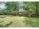 Charming single-story brick home nestled in a lush, green yard with mature landscaping, a carport, and a cheerful blue door at 1403 Dennis Dr, Decatur, GA 30032