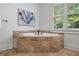 A soaking tub with travertine tile surround is set in front of a sunny window at 1292 Lenox Park Ne Blvd, Brookhaven, GA 30319