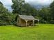Exterior view of a backyard shed with a covered patio, surrounded by lush green grass and trees at 512 Ollas Walk, Mcdonough, GA 30252