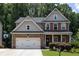 Charming two-story home featuring a two-car garage, stone accents, and a well-maintained front yard with mature trees at 6695 Grove Meadows Ln, Cumming, GA 30028