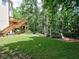 Expansive backyard with lush green grass, mature trees, a wooden deck with stairs, and a play area at 658 Vinings Estates Se Dr, Mableton, GA 30126