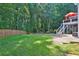 Expansive backyard featuring lush greenery, a wooden fence, and a concrete patio beneath a deck and stairs at 1875 Edgemont Ct, Cumming, GA 30041