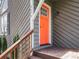 Close up of a bright orange front door, complemented by neutral siding and wood railing steps at 4679 Candlewyck Way, Buford, GA 30518