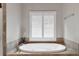 Relaxing bathtub nook with a shuttered window and plant, surrounded by tile and features gold fixtures at 2845 Aquitania Ln, Cumming, GA 30040