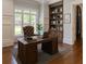 Home office features a wooden desk, built-in bookcase, hardwood floors, and natural light from a large window at 10745 Shallowford Rd, Roswell, GA 30075