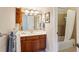 Bright bathroom features a cherry vanity, a sink with stainless steel fixtures, a decorative mirror, and a shower with tile surround at 1382 Murrays Loch Nw Pl, Kennesaw, GA 30152