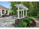 Landscaped patio features a white pergola, brick base, an outdoor dining set, lush landscaping, and mature trees at 1382 Murrays Loch Nw Pl, Kennesaw, GA 30152