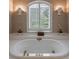 Close up shot of a luxurious soaking tub with white tile, shuttered window and sconces at 4310 Granby Way, Marietta, GA 30062
