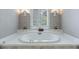 Close up shot of a luxurious soaking tub with white tile, shuttered window and sconces at 4310 Granby Way, Marietta, GA 30062
