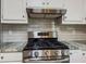 Close-up of stainless steel gas range and hood with granite countertops and white cabinets at 1904 Watercrest Cir, Lawrenceville, GA 30043