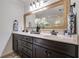 Bathroom featuring double sinks, dark cabinets, granite countertops, and a large framed mirror at 7115 Doncaster Ct, Cumming, GA 30040