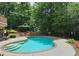 Lush backyard featuring a kidney-shaped pool with a brick border, surrounded by greenery and a wrought iron fence at 215 Settindown Ct, Roswell, GA 30075