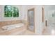 Light-filled main bathroom with a soaking tub, tile surround, glass-enclosed shower, and arched window at 4634 Whitestone Way, Suwanee, GA 30024