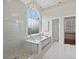 Bright bathroom featuring soaking tub with large window and glass-enclosed shower with marble surround at 1232 Everton Pl, Cumming, GA 30041