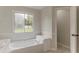 Bright bathroom featuring a large soaking tub beneath a window with a view of the backyard at 250 Meadow View Dr, Grayson, GA 30017