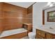 Bathroom with a soaking tub, wood paneling, vanity, and window with a treed view at 6896 Heardsville Rd, Cumming, GA 30028