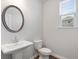 A bathroom with a white pedestal sink, toilet, round mirror, wood-look floors, and window at 6934 Melody Ridge Rd, Buford, GA 30518