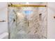 Close-up of a modern shower with white marble-style tiling, glass doors, gold hardware, and mosaic tile floor at 597 Woodcrest Manor Dr, Stone Mountain, GA 30083