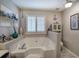 A bathroom featuring a white tub beneath a window with privacy shutters and a gray tiled floor at 263 Bennett Farms Trl, Acworth, GA 30102