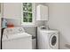 A laundry room with white walls and cabinets, a window, and a side-by-side washer and dryer at 878 Treadstone Overlook, Suwanee, GA 30024