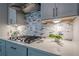 Kitchen cooktop featuring a stone backsplash, white cabinets, and stainless steel vent at 10865 Glenhurst Pass, Duluth, GA 30097
