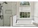 Bright bathroom with a modern bathtub, and a glass-enclosed shower with black trim adjacent to a window at 4944 Dovecote Trl, Suwanee, GA 30024