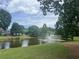 Scenic pond featuring a fountain, set against a backdrop of lush trees and a distant home, offering a serene view at 112 Rotherhithe Nw Ln, Marietta, GA 30066