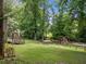 Spacious backyard with lush greenery, mature trees, play set, and a wooden deck with stairs at 992 Marbury Sw Ct, Marietta, GA 30064