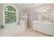 Bright bathroom features tub under arched window, glass shower, and double vanity with white cabinets at 1335 Joy Ct, Suwanee, GA 30024