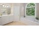 Well-lit bathroom features a soaking tub under an arched window, a white vanity, and tile flooring at 1335 Joy Ct, Suwanee, GA 30024