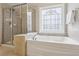 Elegant bathroom featuring a soaking tub with tile surround, a window, and a glass-enclosed shower at 606 Lorimore Pass, Canton, GA 30115