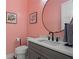 Stylish powder room featuring a round mirror, grey vanity, and trendy light pink walls, enhanced with flower art at 5315 Hendrix Rd, Cumming, GA 30040