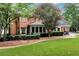 The rear of a brick house features a stone patio and manicured lawn, with lush landscaping and mature trees at 1320 Northcliff Trce, Roswell, GA 30076