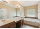 Bathroom features a soaking tub, double vanity, large mirror, and neutral earth-tone tile at 5060 Windcrest Lane, Alpharetta, GA 30022
