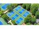 Aerial view of the neighborhood tennis courts features a blue and green surface and surrounded by lush landscaping at 6930 Wesley Hughes Rd, Cumming, GA 30040