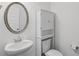 This powder room features a pedestal sink, round mirror, and a white cabinet above the toilet at 230 Waters Edge Pkwy, Temple, GA 30179