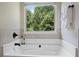 Bright bathroom with a large tub and a window overlooking lush greenery at 1496 Clarecastle Ln, Buford, GA 30519