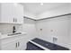 Bright laundry room featuring white cabinets, a sleek marble countertop, black hardware, and herringbone tile floors at 3205 Bold Springs Rd, Dacula, GA 30019