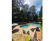 Backyard view of kidney-shaped pool with lounging area, umbrellas, and privacy fence surrounded by mature trees at 60 Stonehedge Dr, Buford, GA 30518