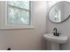 This powder room includes a pedestal sink with dark fixtures, complemented by a round mirror and a window offering natural light at 2346 Hampton Park Dr, Buford, GA 30519