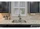 Close-up of a kitchen sink with stainless fixtures and tile backsplash and white shutters at 4814 Little Cove Ct, Auburn, GA 30011